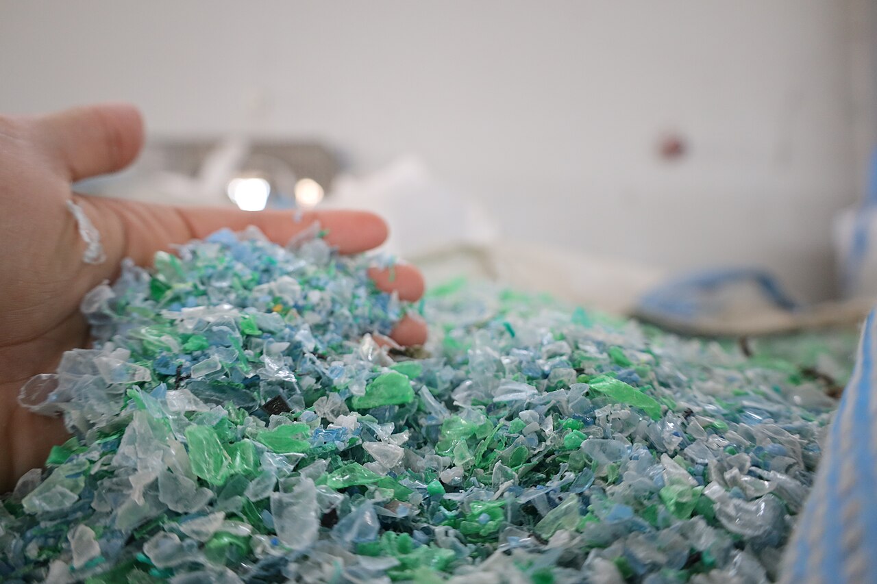 A hand holds a heap of shredded plastic bottle flakes in clear, blue and green.