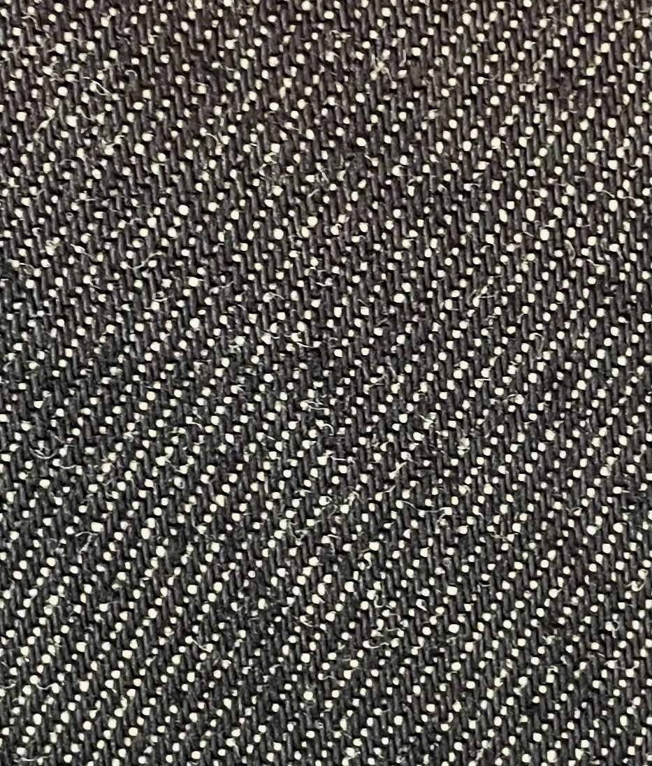 A close-up of unwashed indigo denim, the surface dark blue and flecked with small white points, with a clear diagonal ridge running across the whole frame.
