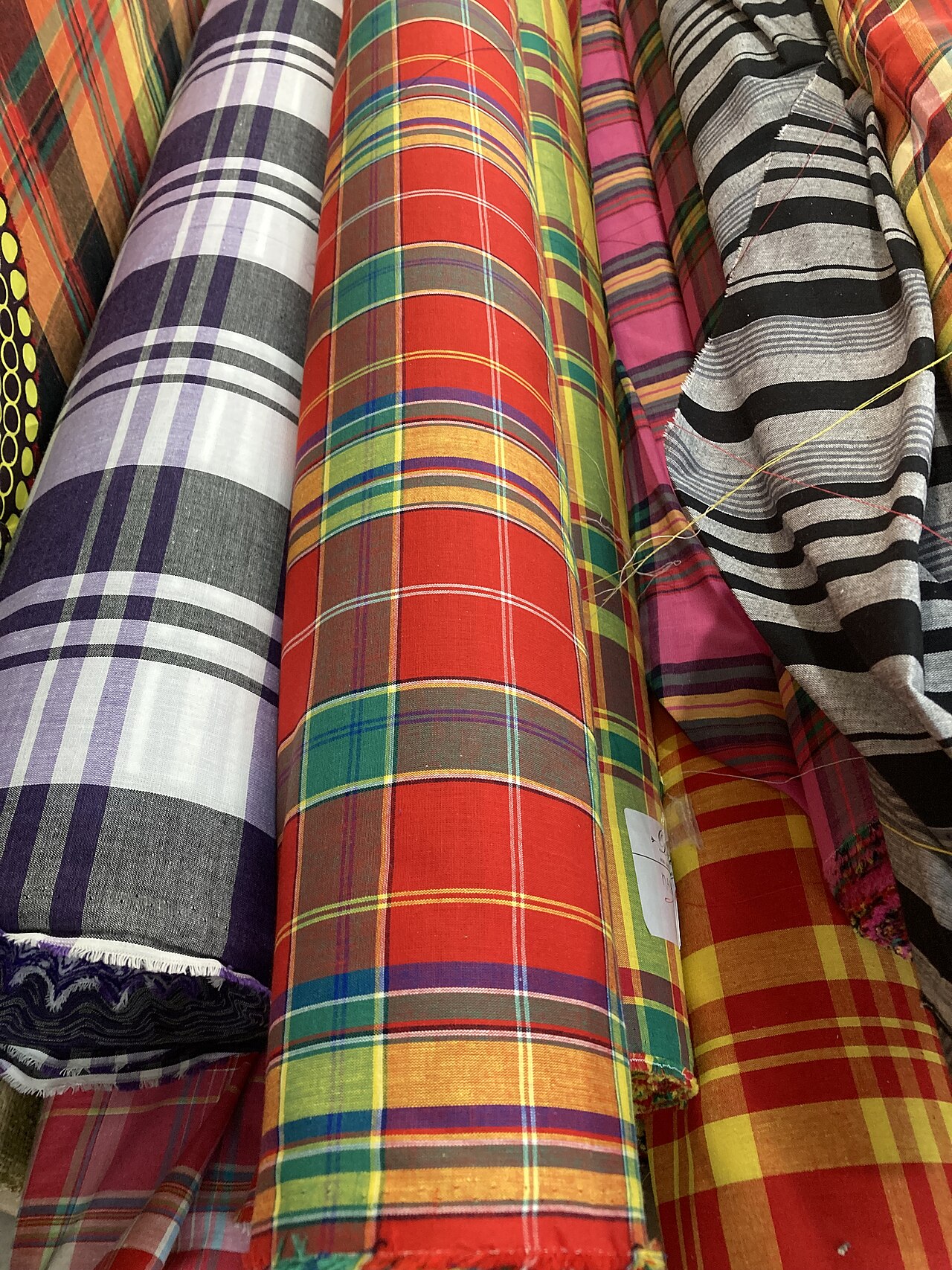 Rolls of madras check and striped cotton cloth stacked together, seen close up.