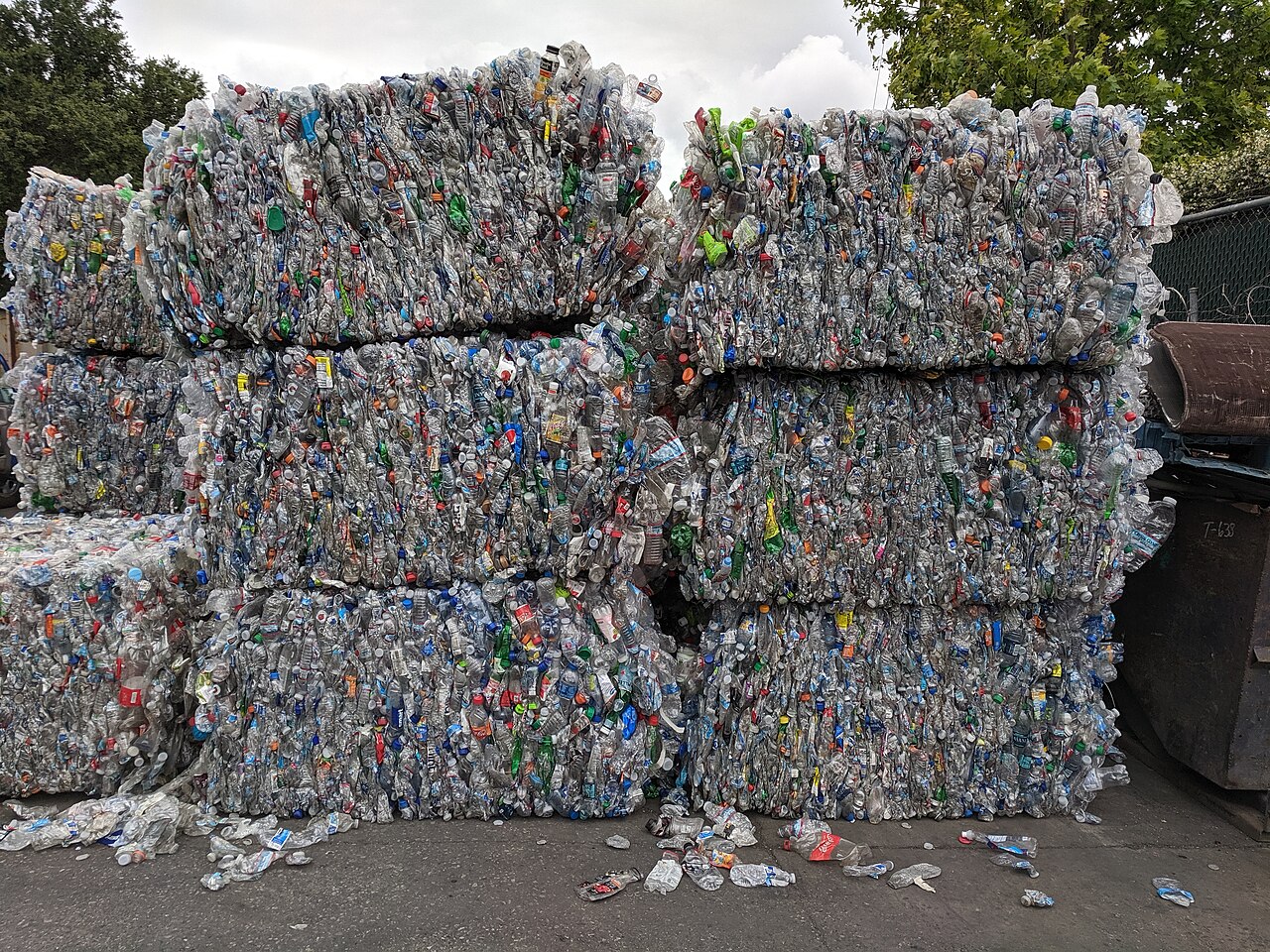 Stacked bales of crushed plastic drink bottles at a recycling yard, wire-bound, thousands of bottles pressed together.